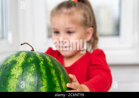 la bambina tocca un grande angurello e sorride mentre aspetta Foto Stock