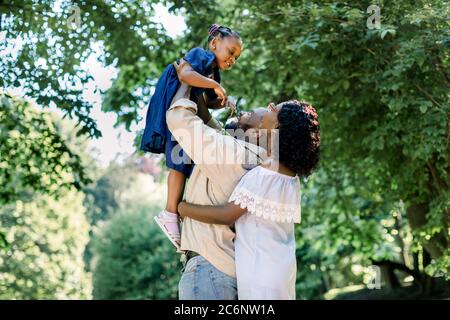 Estate di felice famiglia africana che gioca nel parco. Ritratto di famiglia con persone felici sorridenti al parco, padre solleva la bambina carina Foto Stock