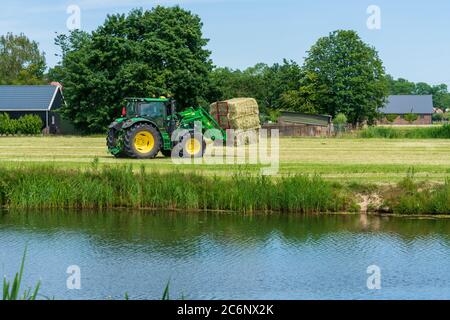 Dordrecht, Paesi Bassi - 1 giugno 2020: Trattore verde che carica balle di fieno su un rimorchio nella campagna rurale. Il Parco Nazionale di Biesbosch è uno dei più grandi parchi nazionali dei Paesi Bassi Foto Stock