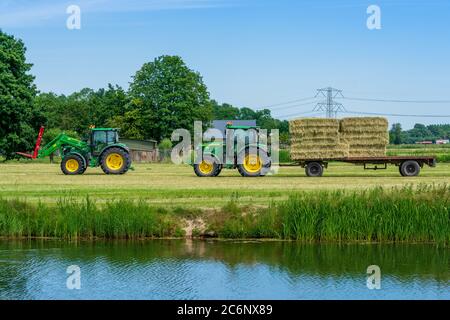 Dordrecht, Paesi Bassi - 1 giugno 2020: Trattore verde che carica balle di fieno su un rimorchio nella campagna rurale. Il Parco Nazionale di Biesbosch è uno dei più grandi parchi nazionali dei Paesi Bassi Foto Stock