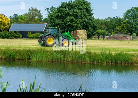 Dordrecht, Paesi Bassi - 1 giugno 2020: Trattore verde che carica balle di fieno su un rimorchio nella campagna rurale. Il Parco Nazionale di Biesbosch è uno dei più grandi parchi nazionali dei Paesi Bassi Foto Stock