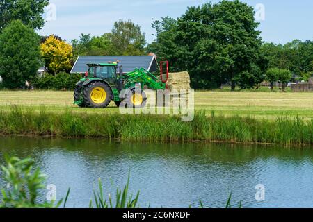 Dordrecht, Paesi Bassi - 1 giugno 2020: Trattore verde che carica balle di fieno su un rimorchio nella campagna rurale. Il Parco Nazionale di Biesbosch è uno dei più grandi parchi nazionali dei Paesi Bassi Foto Stock