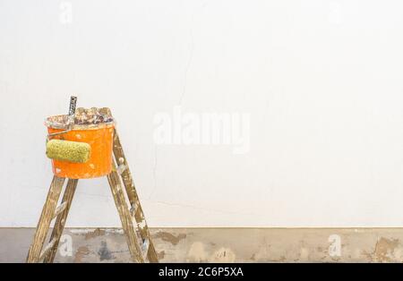 Sfondo miglioramento casa con scala, secchio e rullo di vernice davanti ad una parete bianca esterna Foto Stock