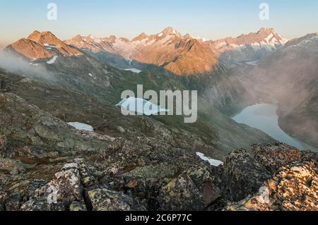 Mentre il Finsteraarhorn e il Lauteraarhorn catturano la prima luce solare, il ghiacciaio Unteraar e il lago Grimsel sottostante sono ancora avvolti nell'oscurità. Foto Stock