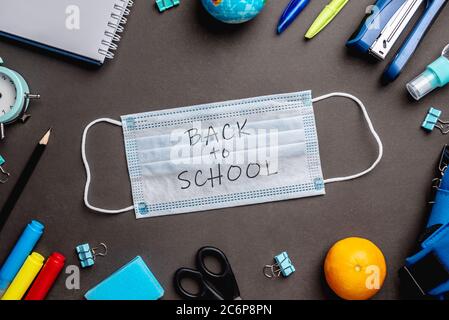 La scuola di cancelleria fornisce intorno alla maschera medica su sfondo nero. Vista dall'alto. Concetto di ritorno a scuola. Foto Stock