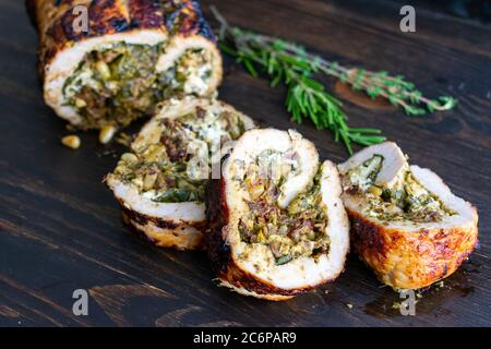 Tenderloin di maiale farcito mediterraneo: Maiale arrosto farcito con spinaci, pesto e formaggio di capra su sfondo di legno scuro Foto Stock