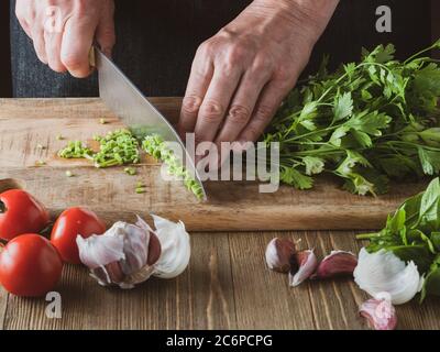 Donna che trita mazzo di prezzemolo su un tagliere di legno. Foto Stock