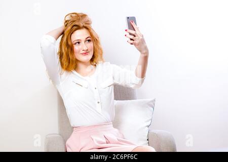 Donna che usa il telefono cellulare per la chat video online su bianco. Donna allegra che tiene il telefono cellulare sorridendo sulla fotocamera mentre prende selfie, facendo videochiamata Foto Stock