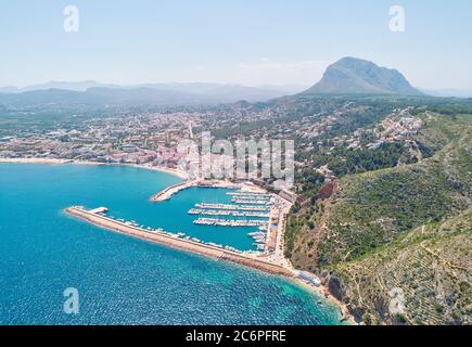 Foto aerea drone punto di vista costiera città di Javea con montagne verdi, turchese baia Mediterraneo Mare ormeggiato navi nel porto, Spagna Foto Stock