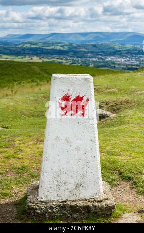 Il trig o punto di triangolazione sulla cima di Mynydd Illtyd nel Beacons centrale di Brecon a Powys nel Galles del sud, con un drago gallese dipinto su. Foto Stock