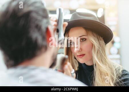 Donna barbiere taglio e taglio barba di cliente nel suo negozio Foto Stock