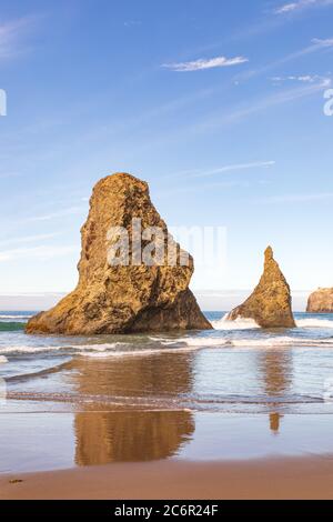 Immagine verticale - due pile di mare che si riflettono nell'acqua sulla spiaggia di Bandon in Oregon Foto Stock