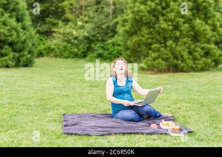 Bella donna incinta sta ridendo in un parco verde estivo con computer portatile e bicicletta. Foto Stock