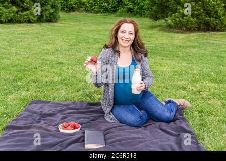 donna incinta con una bottiglia di latte su un campo verde in un parco. Foto Stock