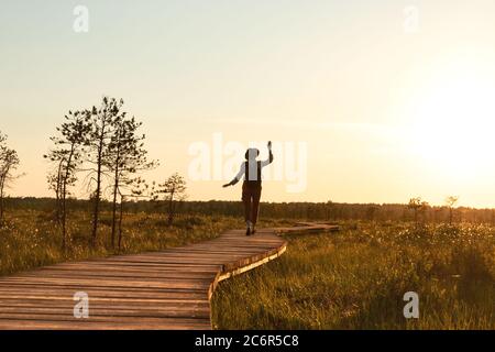Silhouette di donna con zaino su sentieri escursionistici in estate all'aperto. Naturalista gode della natura e un momento al tramonto a piedi sul sentiero attraverso torba Foto Stock