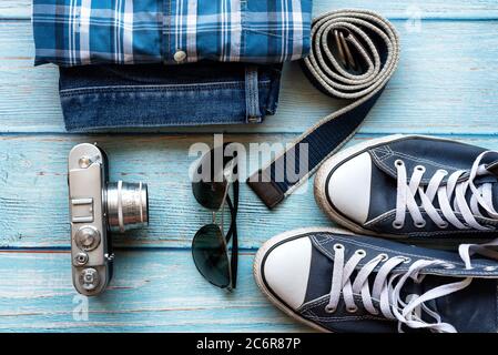 Set di abbigliamento e accessori da uomo, piatto. Concetto di hipster. Abiti casual da uomo, sneakers blu, blu jean, occhiali da sole vecchia macchina fotografica, cintura blu Foto Stock