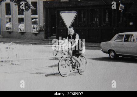 Fine anni '70 vintage nero e bianco stile di vita fotografia di una donna che cavalcano la sua bicicletta in strada. Foto Stock