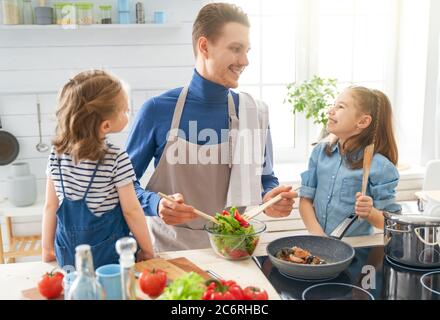 Cibo sano a casa. Famiglia felice in cucina. Padre e figlie stanno preparando un pasto adeguato. Foto Stock