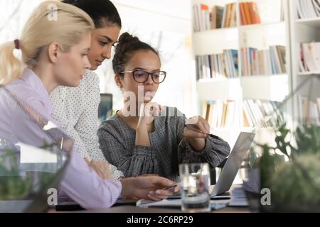 I dipendenti donne multirazziali concentrati collaborano al computer portatile in ufficio Foto Stock