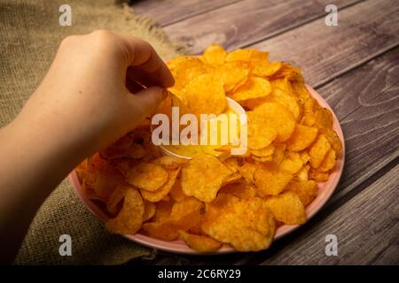 La ragazza prende un chip da un piatto rotondo con patatine e una pentola con salsa di formaggio al centro del piatto. Primo piano Foto Stock