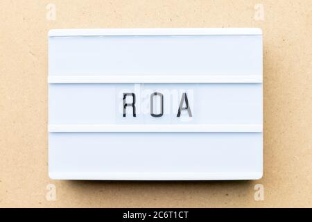 Scatola luminosa bianca con la parola ROA (Abbreviazione del ritorno sugli asset) su sfondo di legno Foto Stock