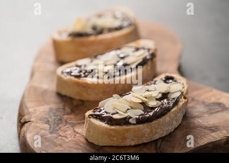 Ciabatta rustica con crema di cioccolato organico e scaglie di mandorle su tavola di ulivo, fuoco basso Foto Stock