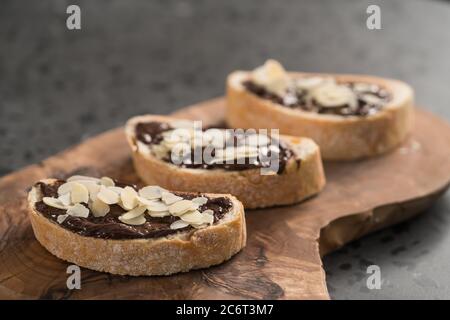 Ciabatta rustica con crema di cioccolato biologica e fiocchi di mandorle tavola di legno di oliva Foto Stock