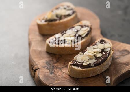 Ciabatta rustica con crema di cioccolato biologica e fiocchi di mandorle tavola di legno di oliva Foto Stock