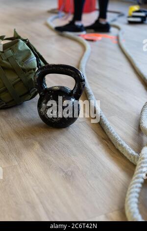 Attrezzature da palestra per il campo di stivali e allenati con il bicchiere del bollitore, la corda, la borsa da sabbia nella palestra sul pavimento. Gambe dell'istruttore sullo sfondo. Shot verticale. Foto Stock