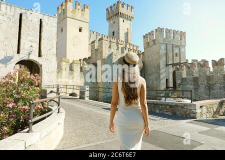 Viaggi in Italia. Indietro veduta di una donna turistica che cammina a Sirmione verso il Castello Scaligero. Vista posteriore di ragazza che si gode in visita Europa. Foto Stock