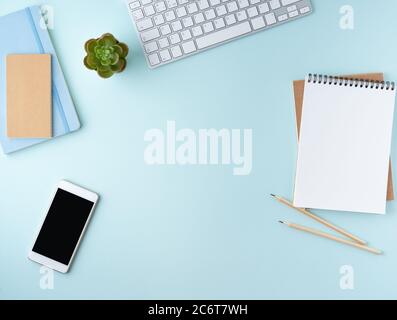 Vista dall'alto del moderno desktop blu per ufficio con blocco note vuoto, computer e smartphone. Mock up Foto Stock