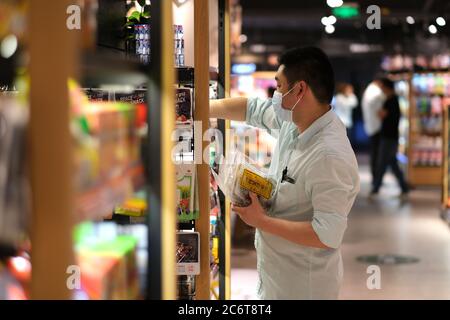 impiegato del supermercato che fissa il cibo sul ripiano, indossando la maschera facciale per evitare il coronavirus covid-19 Foto Stock