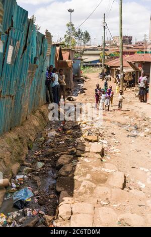 Bambini che giocano su un vicolo sterrato con fogna aperta piena di rifiuti accanto a loro, Korogocho slum, Kenya, Africa orientale Foto Stock