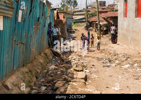 Bambini che giocano su un vicolo sterrato con fogna aperta piena di rifiuti accanto a loro, Korogocho slum, Kenya, Africa orientale Foto Stock