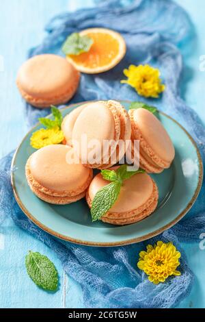 Amaretti dolci d'arancio su tavola blu e fiori gialli Foto Stock