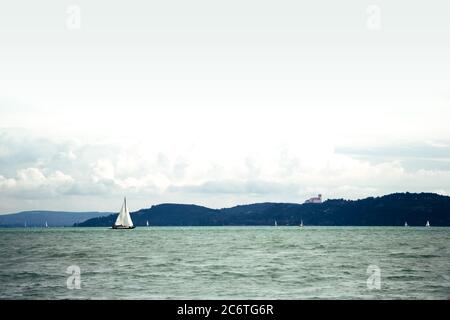 barca a vela bianca in un pomeriggio estivo nuvoloso al Lago Balaton con colline Tihany sullo sfondo. Balaton è il più grande lago dell'Europa centrale. Foto Stock