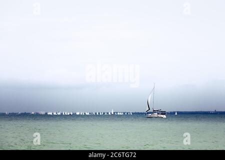 Vista panoramica sul lago Balaton con barche a vela bianche e montagne blu in un pomeriggio estivo nuvoloso. Balaton è il più grande lago dell'Europa centrale Foto Stock