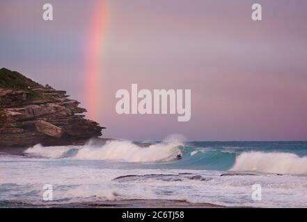 Un bodyboarder solista si surfà una pausa sulla barriera corallina vicino a Tamarama Beach a Sydney sotto un cielo arcobaleno Foto Stock