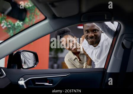 giovane coppia africana è interessata all'auto, guardano la macchina fotografica attraverso la finestra di auto, sorriso Foto Stock