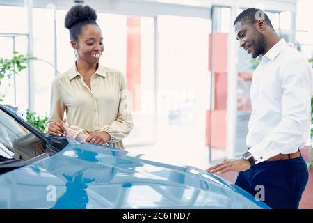 coppia nera in contemplazione prima di fare l'acquisto in showroom automobili, discutono insieme, guardano l'auto blu di lusso e parlano Foto Stock