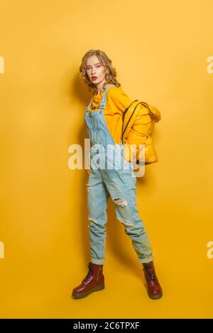 Donna di moda con giacca in piumino e jumpsuit in denim su sfondo giallo brillante Foto Stock