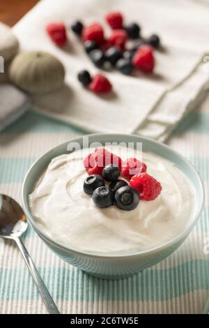 Ciotola di berries e yogurt freschi misti servita su un panno azzurro e bianco e Tovaglia bianco con lamponi e mirtilli su di esso Foto Stock