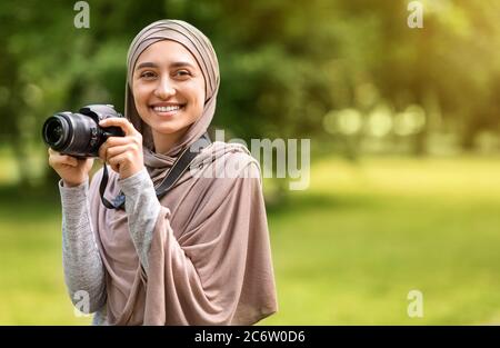 Bella donna musulmana fotografo con fotocamera digitale al parco Foto Stock