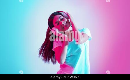 Godetevi la danza. Happy asian ragazza tiene le mani sulle cuffie e ascolta la musica Foto Stock