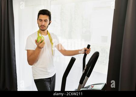 Un uomo entra per lo sport a casa durante la quarantena. Un giovane uomo è impegnato su un simulatore senza andare fuori. Foto Stock