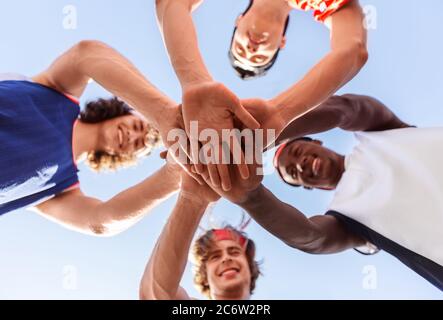 Sportivi multirazziali mettendo le mani insieme prima di giocare a basket all'aperto, vista dal basso Foto Stock