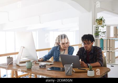 Ritratto di due giovani sviluppatori IT che lavorano insieme al progetto mentre si siedono alla scrivania e si utilizzano computer in interni moderni dell'ufficio, spazio di copia Foto Stock