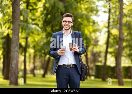 Buon lavoratore d'ufficio con il suo caffè mattina controllare le e-mail al telefono al parco il giorno di sole Foto Stock