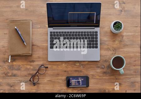 Vista dall'alto sullo sfondo composizione di laptop e smartphone con codice computer su scrivania in legno testurizzato in ufficio, spazio per la copia Foto Stock