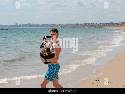 Christchurch, Regno Unito. Domenica 7 luglio 2020. Un giovane porta il suo cane in mare a Hengistbury Head. Credit: Thomas Faull/Alamy Live News Foto Stock